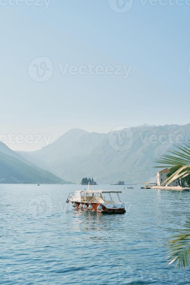 View from the shore of a tourist boat sailing on the sea towards the mountains photo
