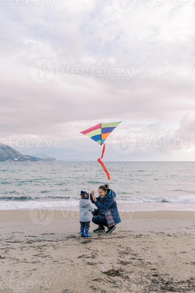 Happy mom crouched next to a little girl with a colorful kite near the sea photo