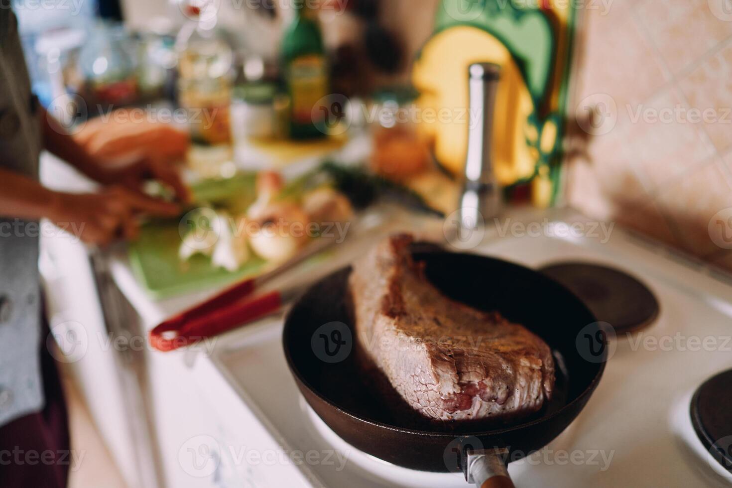 Roast beef is stewed in a pan while the chef cuts vegetables on the table. Cropped photo