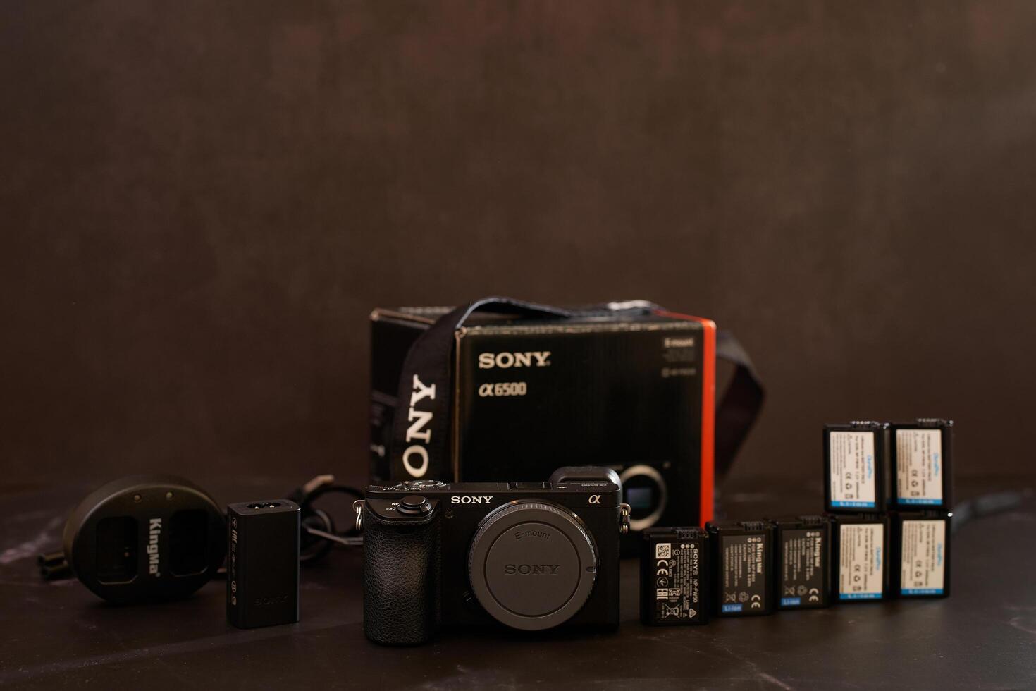 USA, Arizona - March 10, 2025. Sony A6500 mirrorless camera with charger, batteries and strap stands on a black table photo
