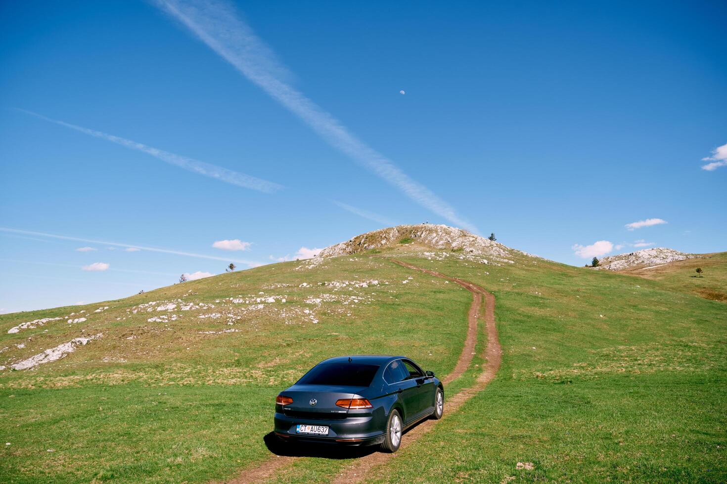 Montenegro, Zabljak - May 09, 2024. Car is driving along a country road on a green plain uphill. Back view photo
