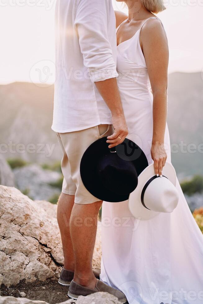 Groom and bride standing in the mountains with hats in their hands. Cropped. Faceless photo
