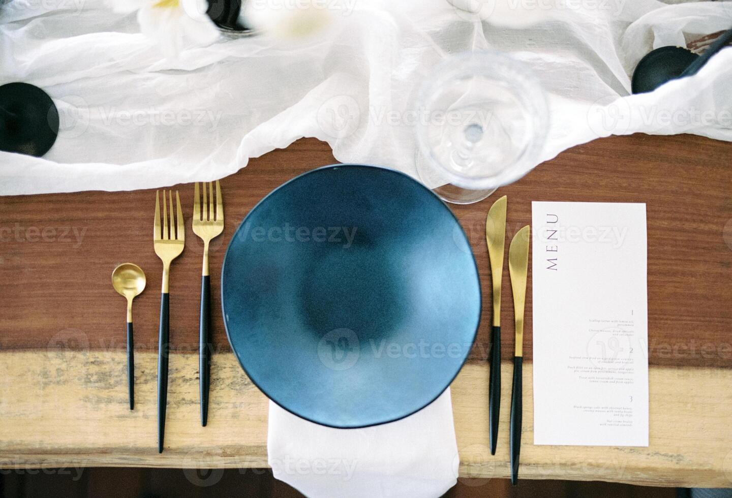 Festive menu lies near a black plate with gold cutlery on a set table. Top view photo
