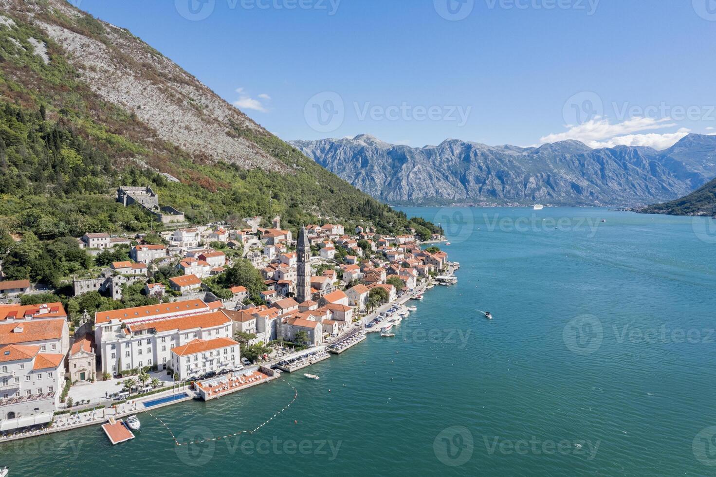 Yacht sails along the coast of Perast with ancient houses and the bell tower of the Church of St. Nicholas. Montenegro. Drone photo