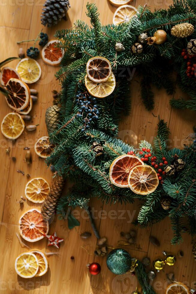 Pieces of dried oranges and fir cones lie near a Christmas wreath on a wooden floor. Cropped photo