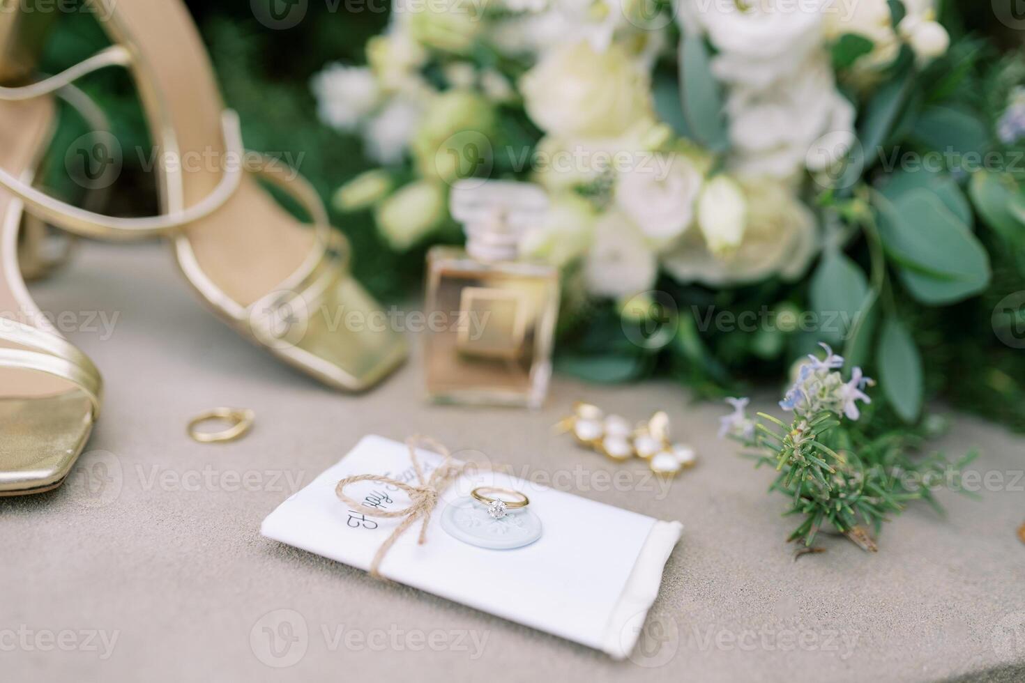 Wedding ring lies on an invitation with a stamp tied with a thread near the bride's shoes photo