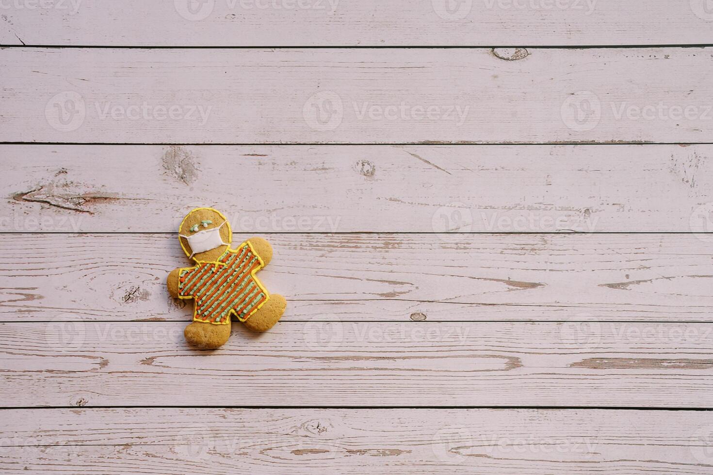 Gingerbread man in a mask lies on the edge on a light wooden background photo