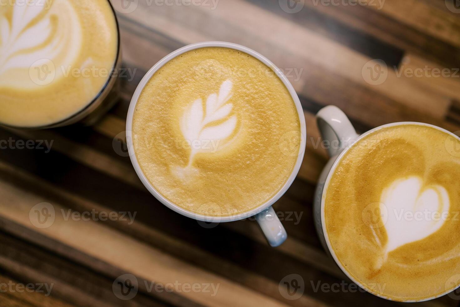 Cups of cappuccino with patterns on the foam stand diagonally on a wooden table. Top view photo