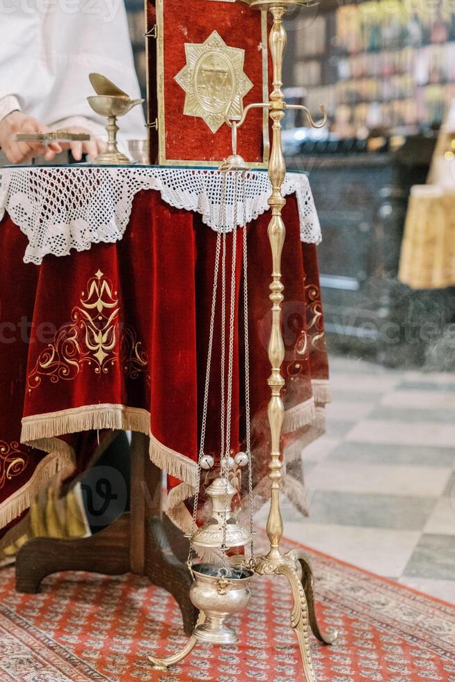 Priest places the cross on the table next to the smoking censer on a stand. Cropped. Faceless photo