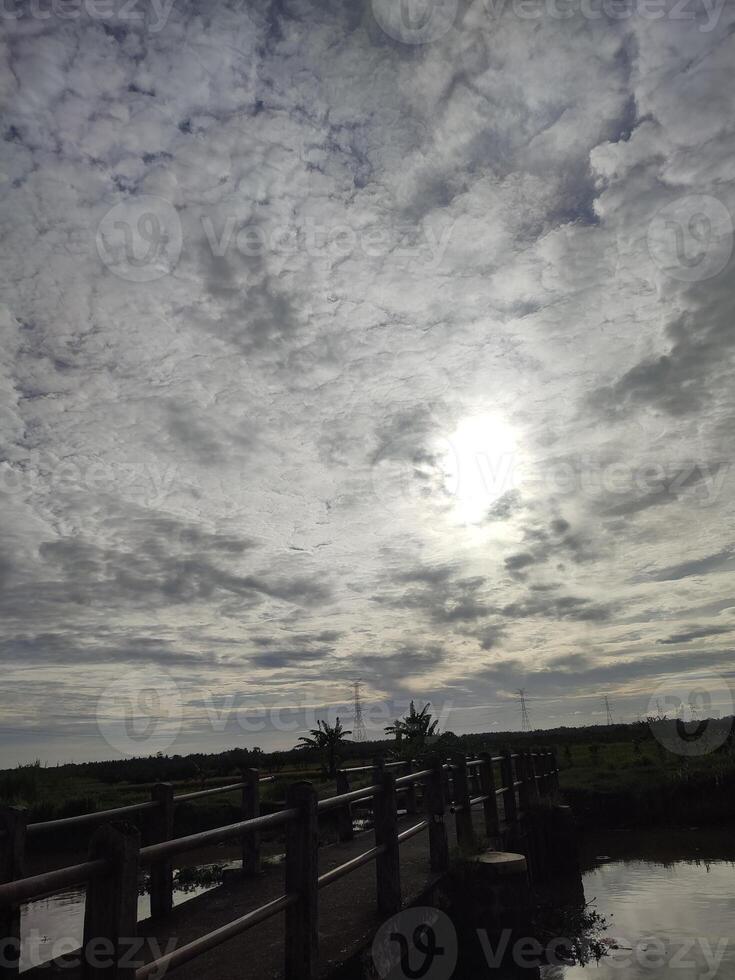 a bridge over a body of water with the sun shining through the clouds photo