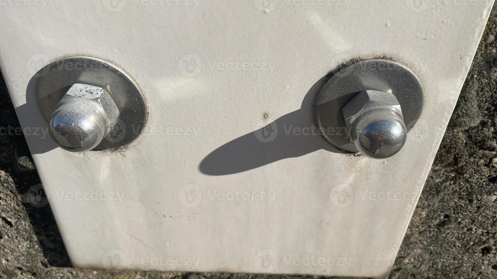 Close-up view of bolts securing a white metal plate to a textured stone wall in bright daylight photo