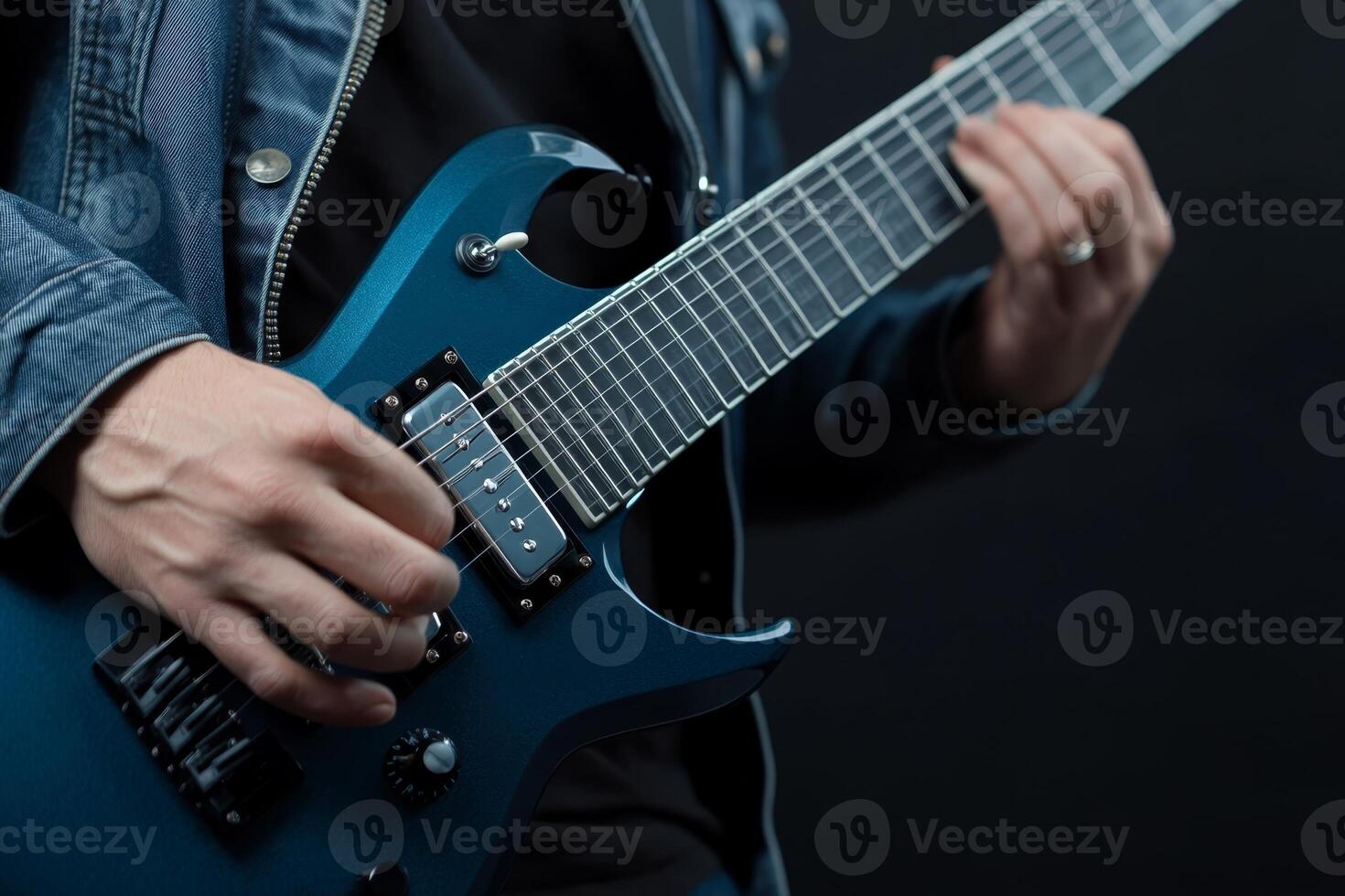 Skilled musician performs with electric guitar wearing denim jacket against dark background photo