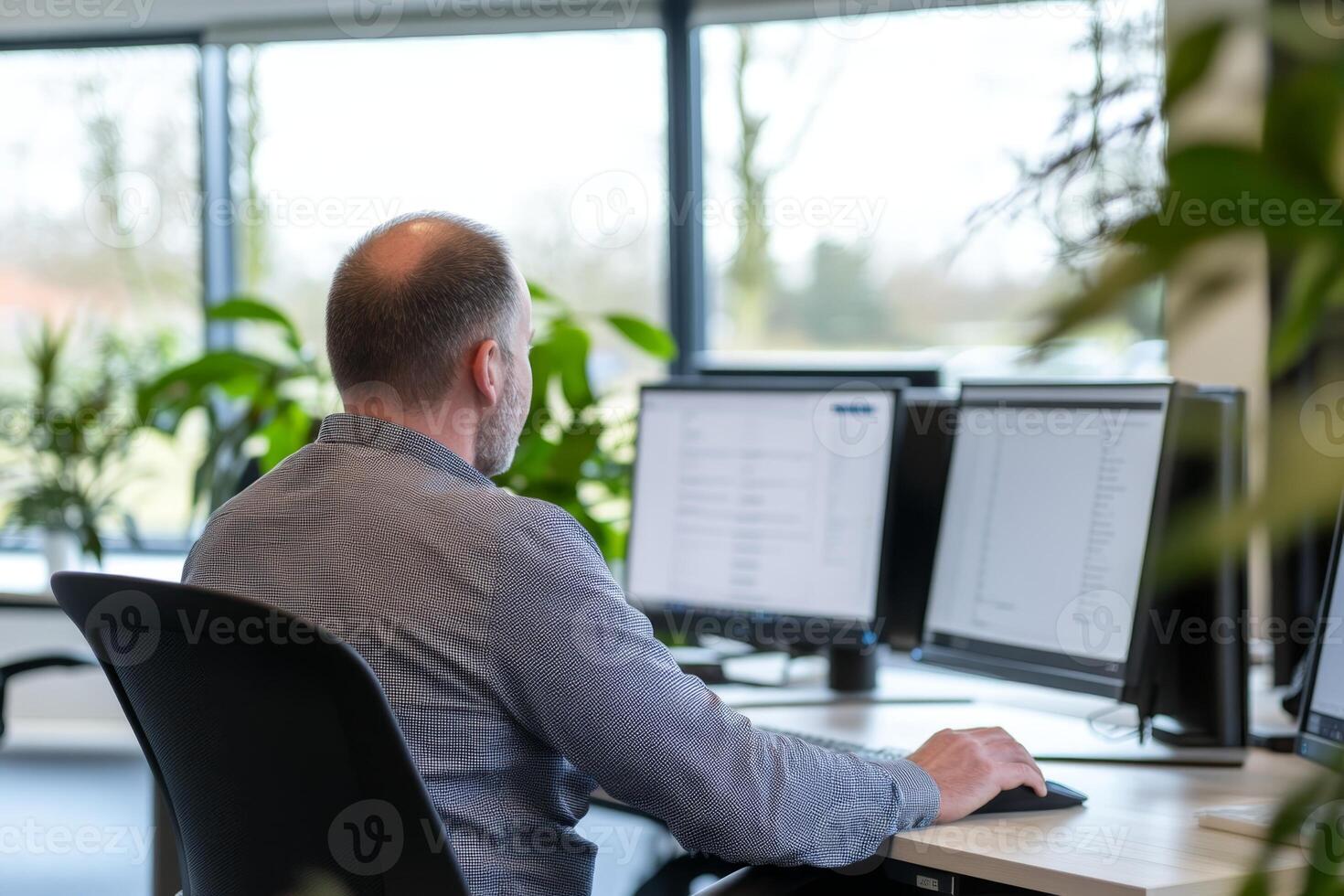 Man working at a desk with multiple monitors in a modern office setting surrounded by greenery photo