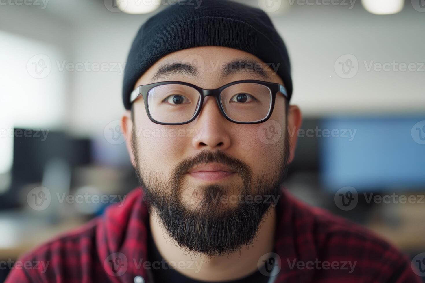 Portrait of a man wearing a beanie and glasses, smiling in a modern workspace during daytime photo
