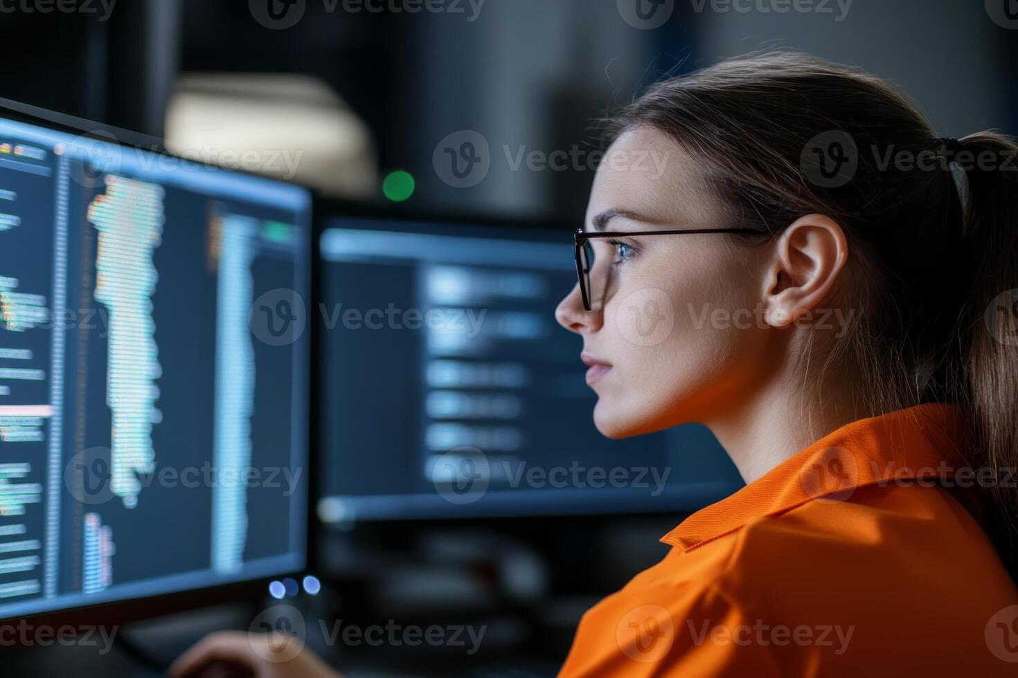 Woman coding in a dimly lit workspace with multiple computer screens displaying programming languages photo