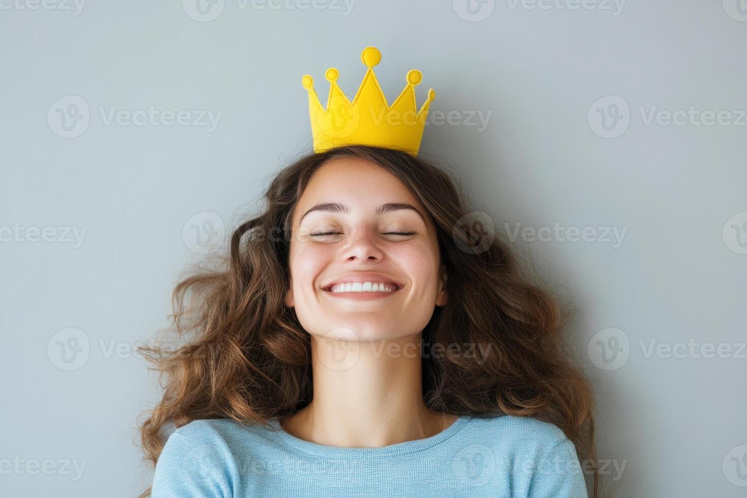 Young woman wearing a yellow crown smiles joyfully against a neutral background at a relaxed indoor setting photo