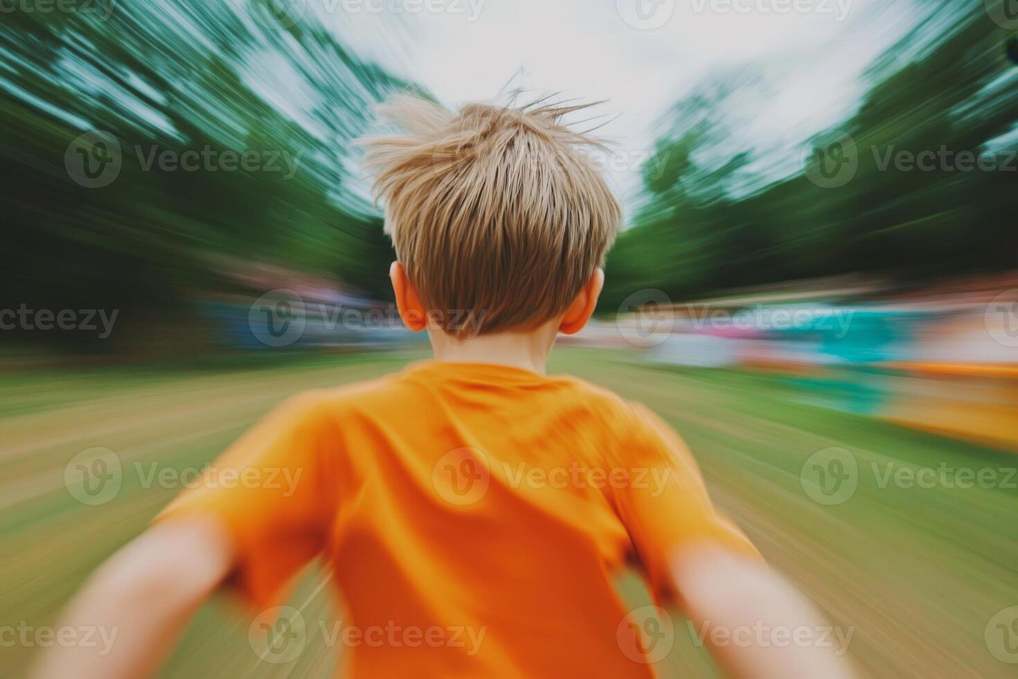 Child joyfully running in a vibrant orange shirt during an outdoor activity in a park on a cloudy day photo