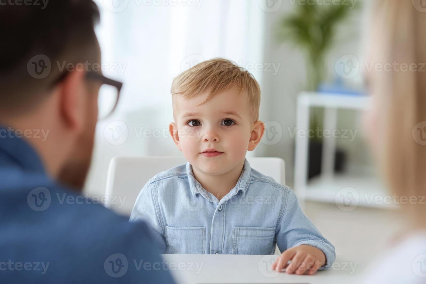 Young boy sitting at a table with parents engaged in conversation in a bright, modern living room photo