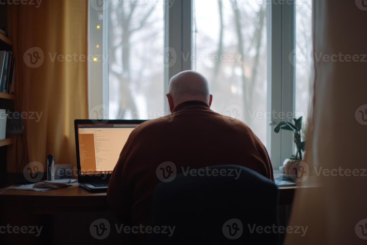Old man working on laptop in cozy indoor workspace during snowy winter morning photo