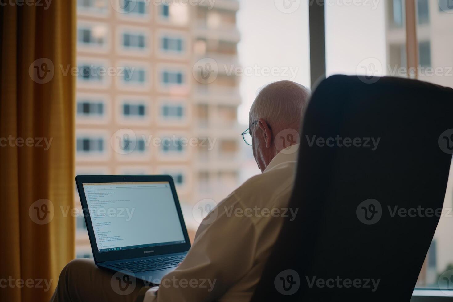 Elderly man working on laptop in cozy room with city view during the day photo
