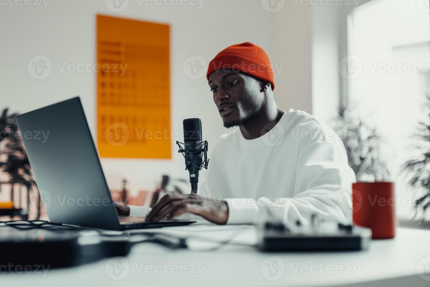 Young man working intently at a laptop in a modern workspace with a microphone and creative elements around photo