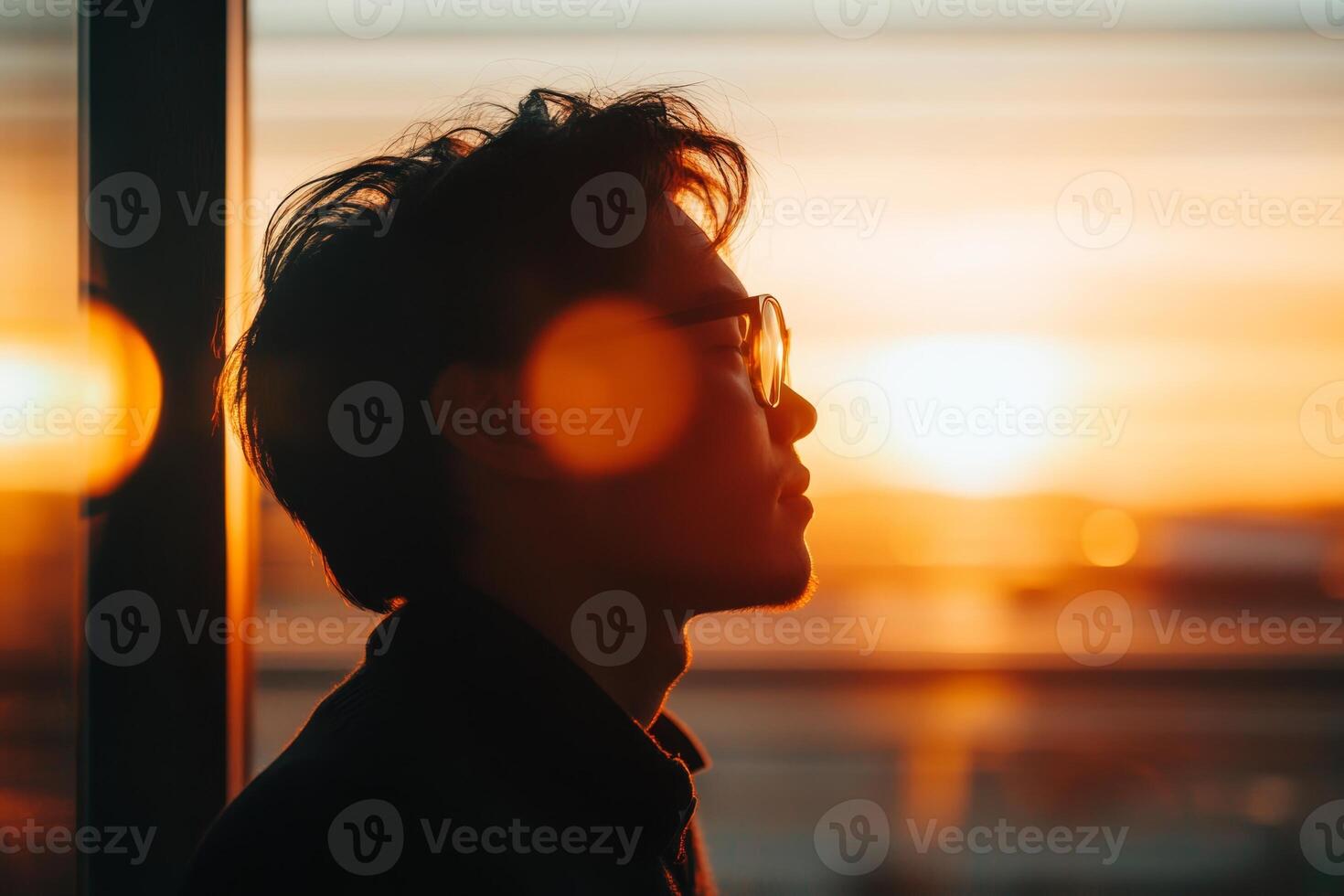 Silhouette of a man gazing at a sunset through a window in a modern urban setting during evening hours photo