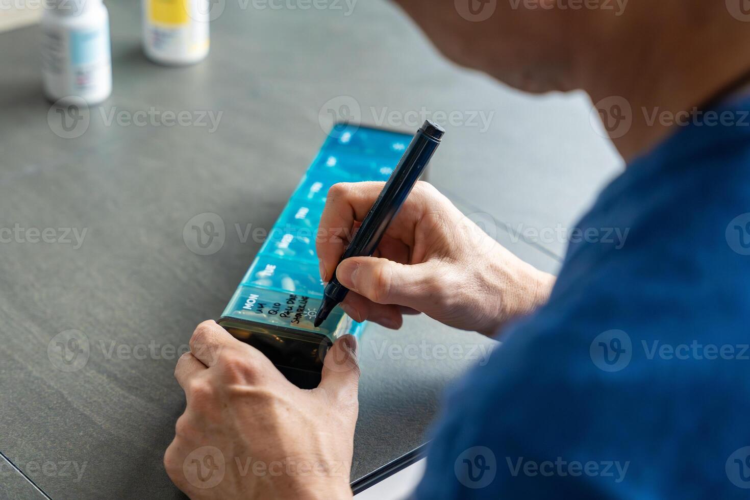 Man labeling compartments of his pill organizer with a permanent marker. Concept of organizing and personalizing medication management. High quality photo