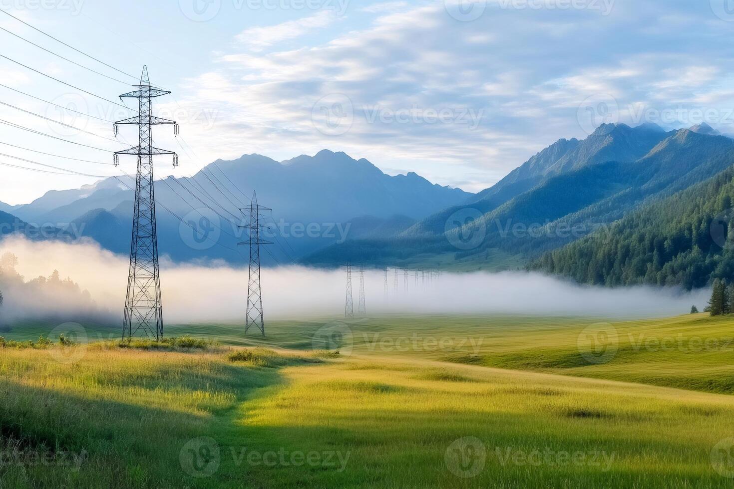Power lines crossing a green meadow with fog in a mountain valley photo