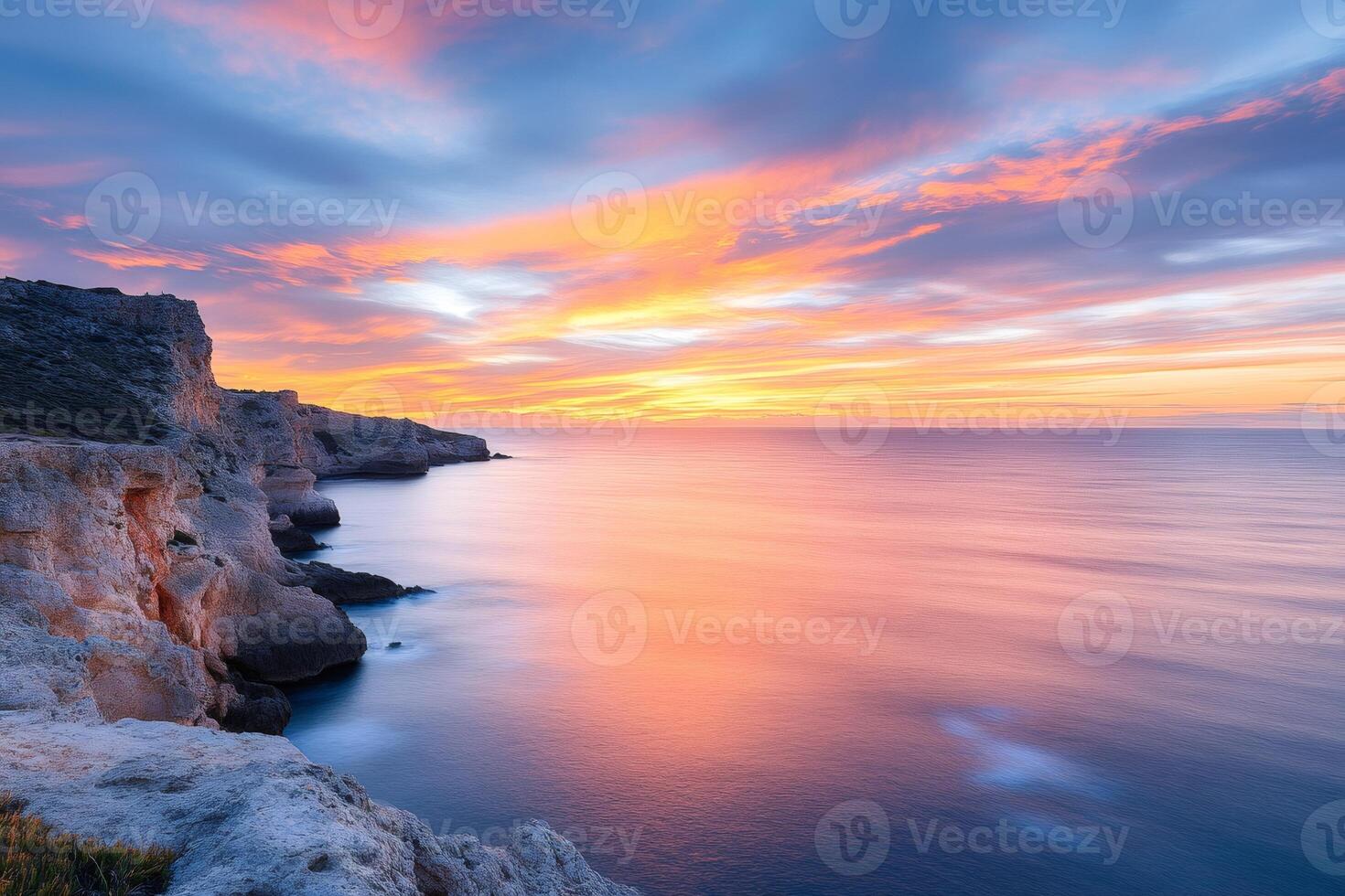 Colorful sunrise illuminating calm ocean and rocky coastline photo