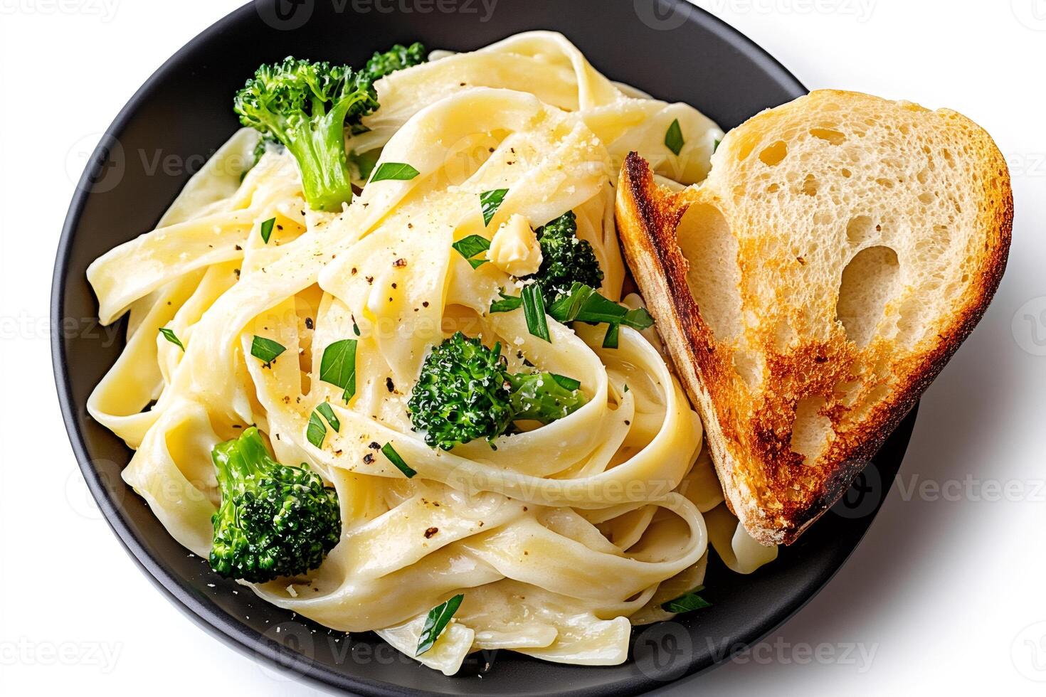 Fettuccine alfredo pasta with broccoli florets and toasted bread in black bowl photo