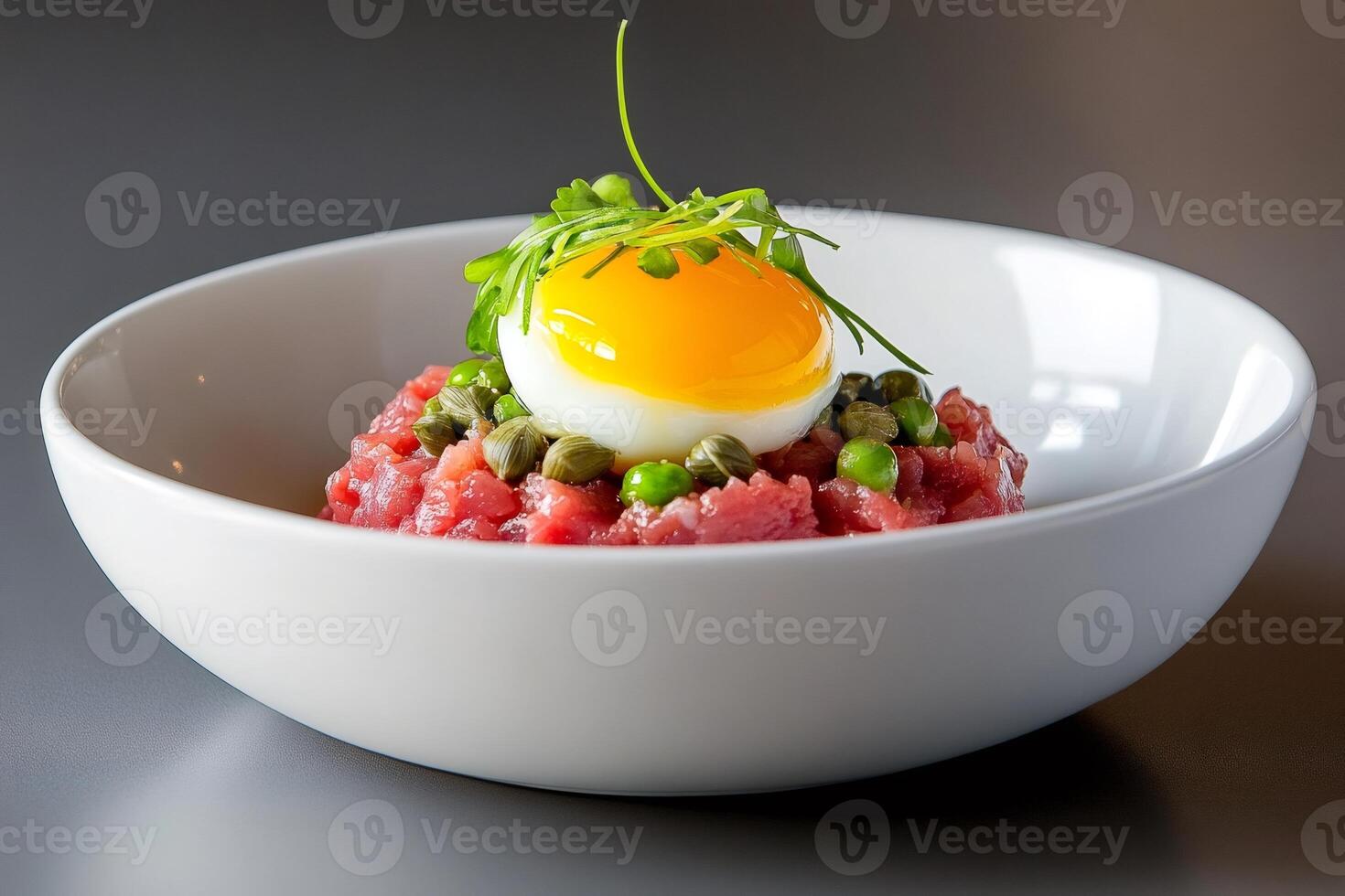 Beef tartare with egg yolk, capers and peas decorating a white bowl photo