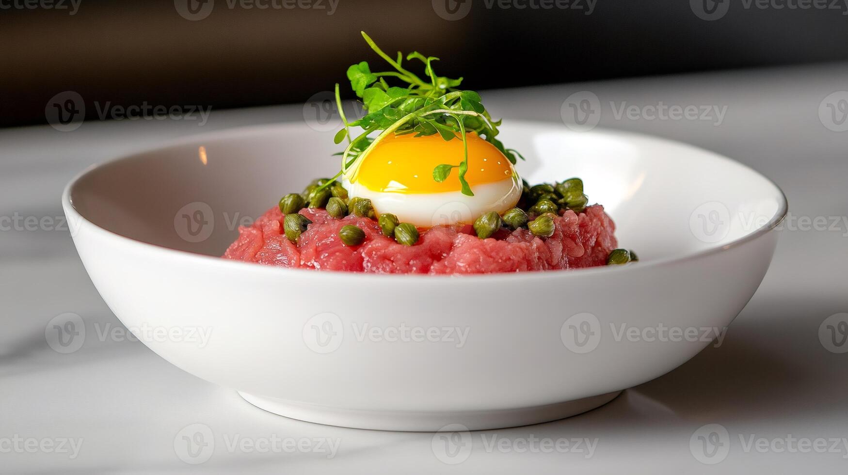 Beef tartare with egg yolk, capers and sprouts decorating a white bowl photo