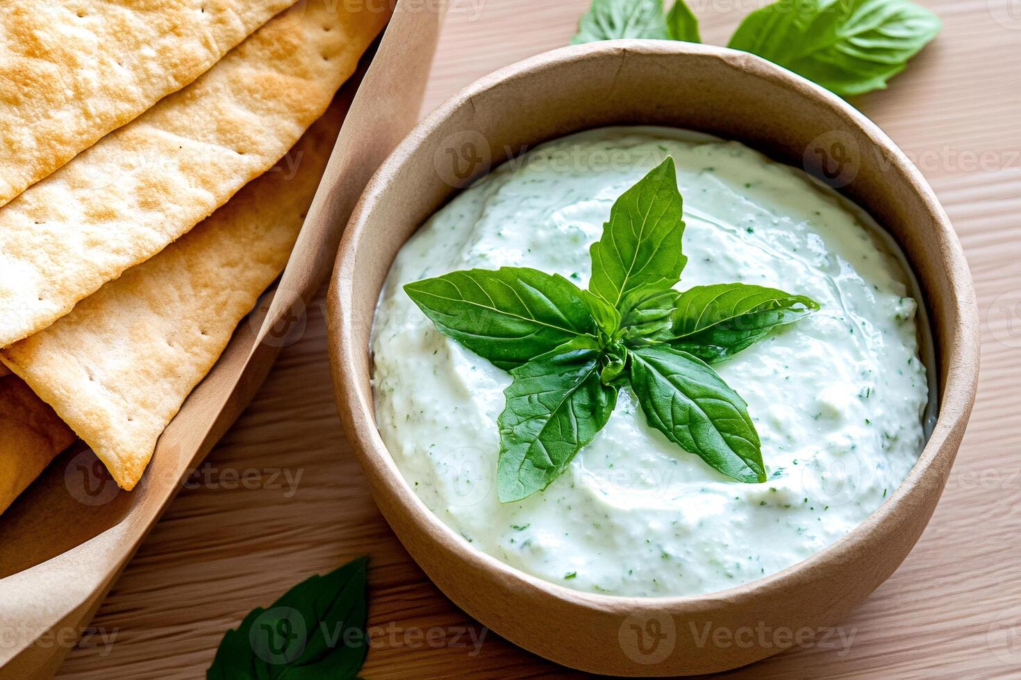 Creamy sauce with basil and crackers decorating wooden table photo