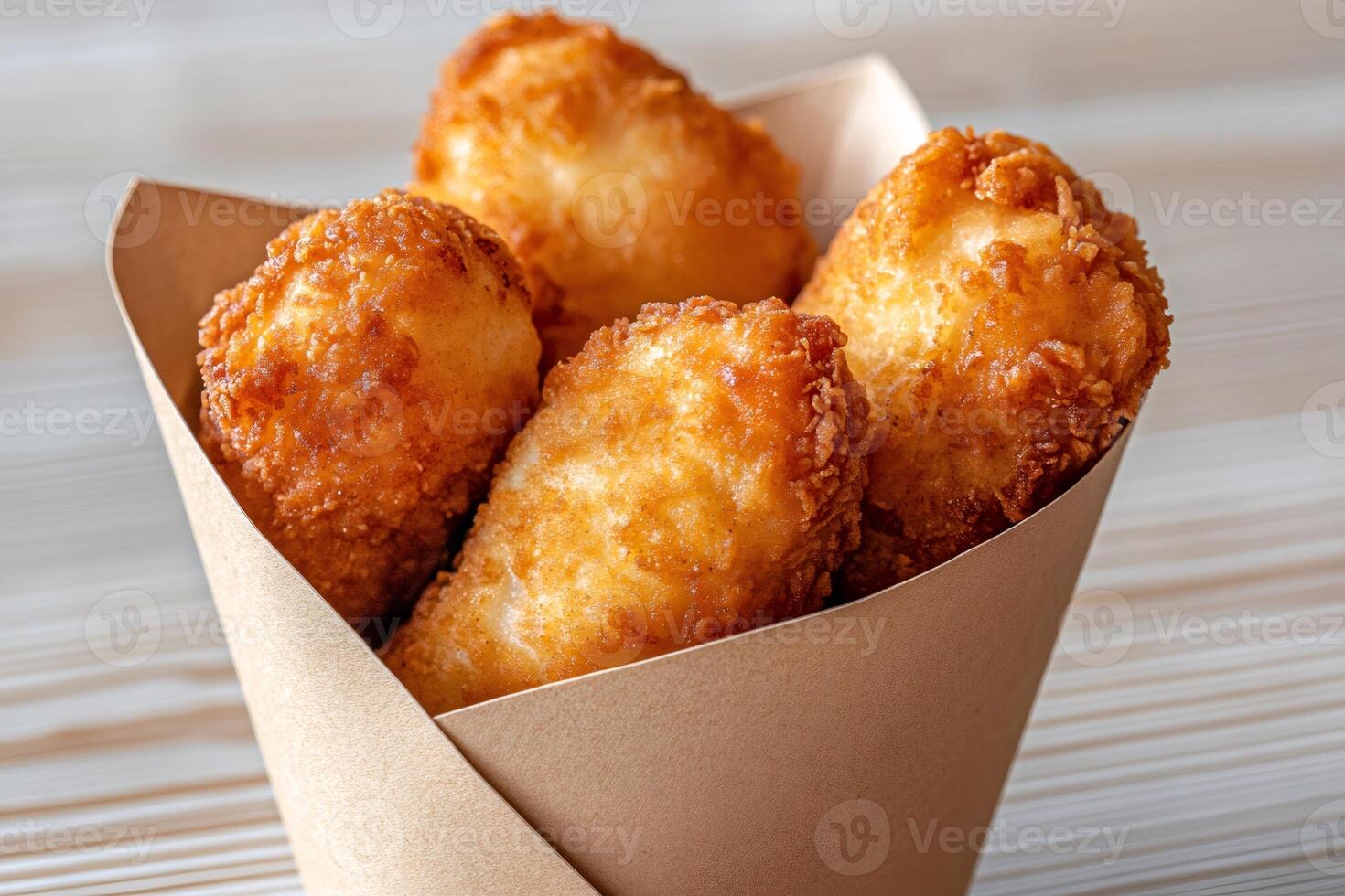Breaded mozzarella sticks overflowing a small paper cone on wooden table photo