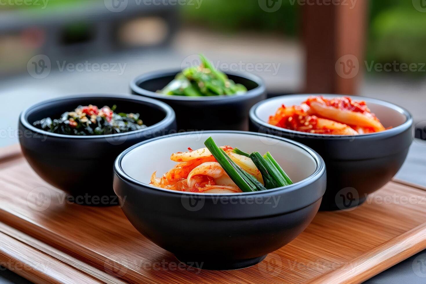 Korean banchan side dishes served in small black bowls on wooden tray photo