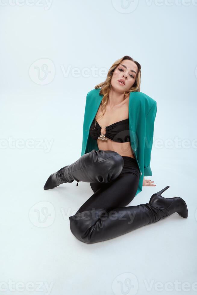 Beautiful girl in a green jacket and black pants sitting on the floor. photo