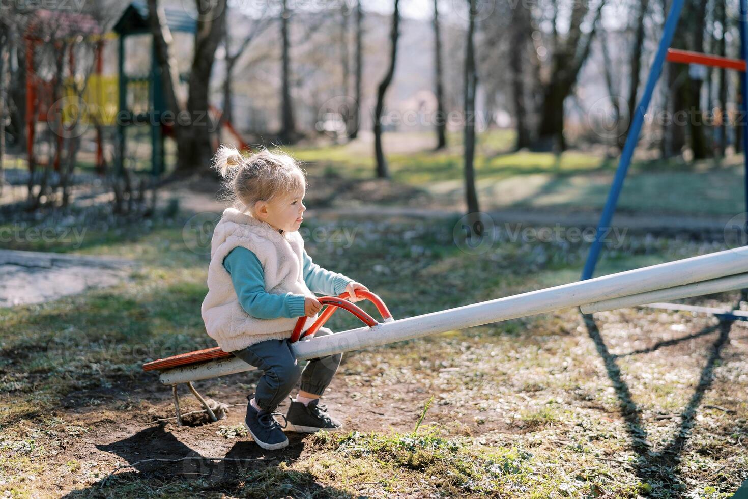 Little girl sits on a swing-balancer holding on to the handles in the playground photo