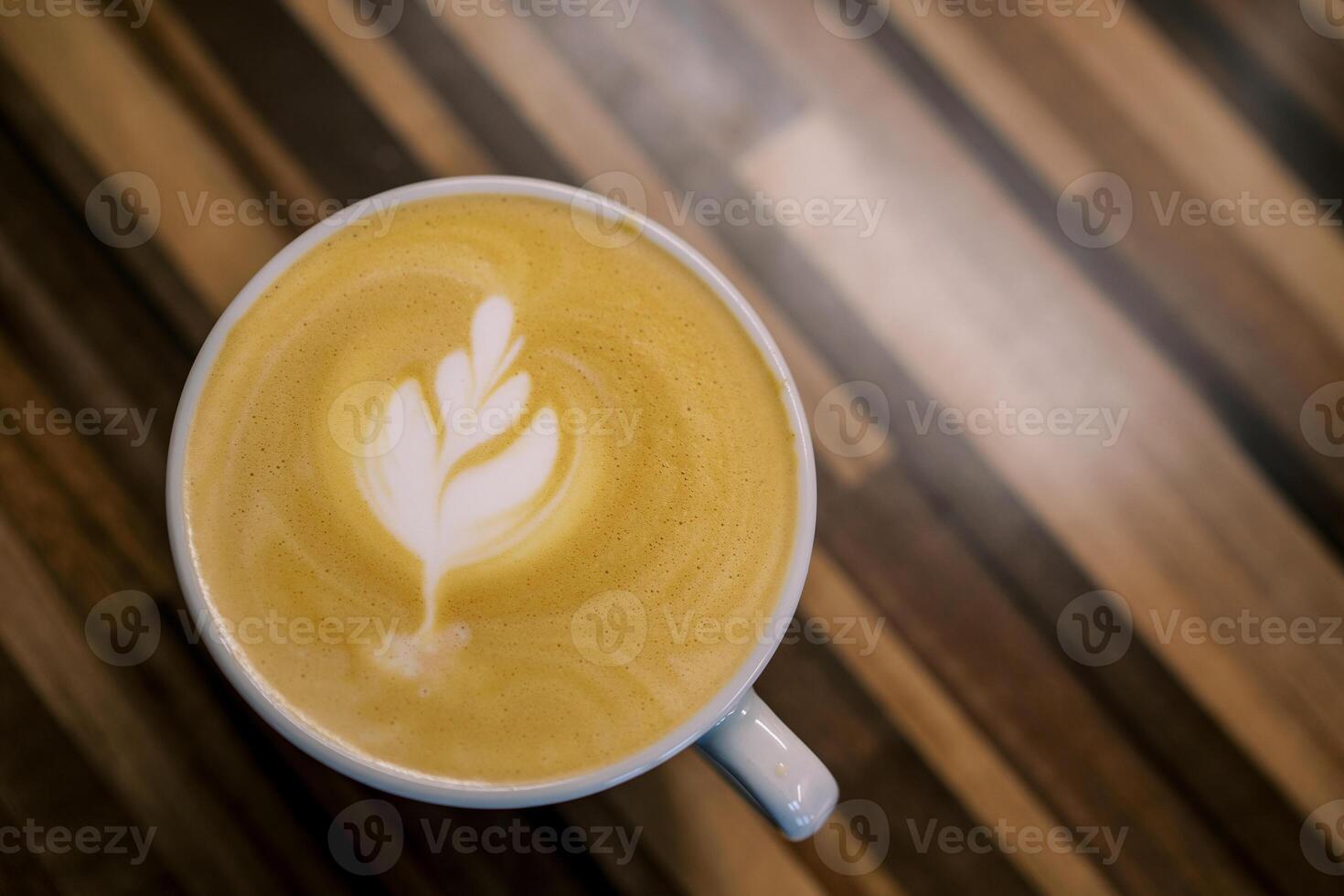 Latte with a leaf on the foam stands in a cup on a wooden table. Top view photo