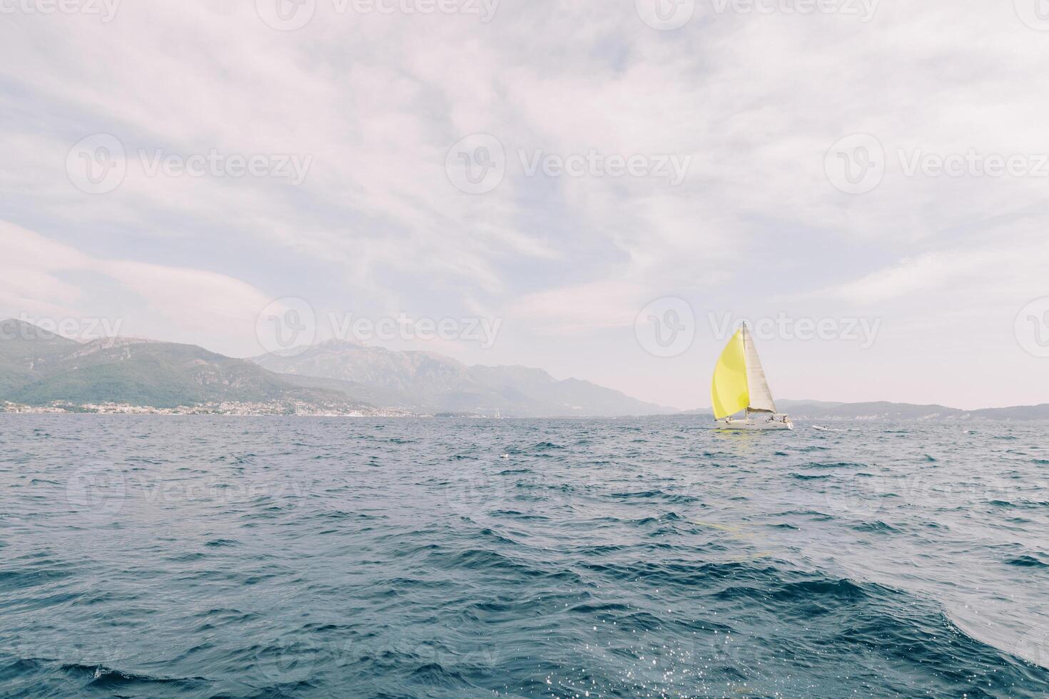 Yellow sailboat sails on the sea against the backdrop of mountains in a light haze photo