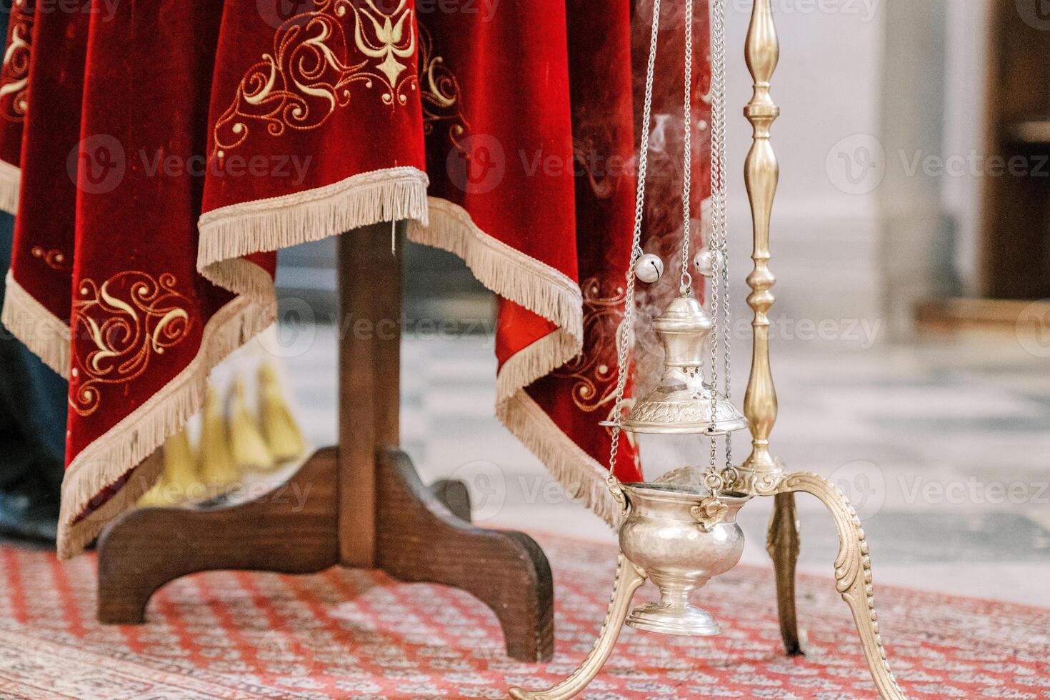 Smoking censer hangs on a gold chain on a stand near a table with a red tablecloth photo