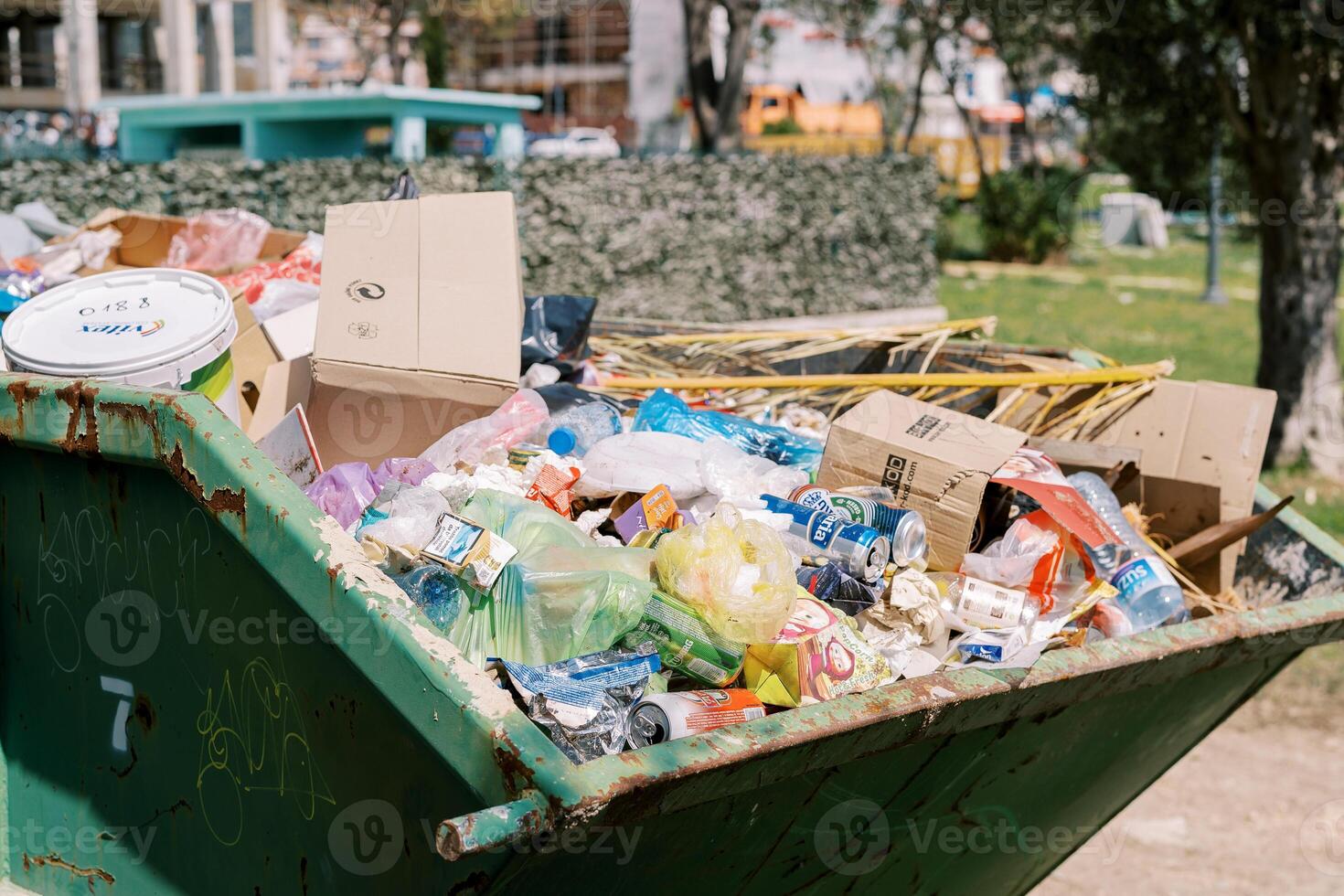 Overflowing metal trash can with garbage in the yard of a house photo