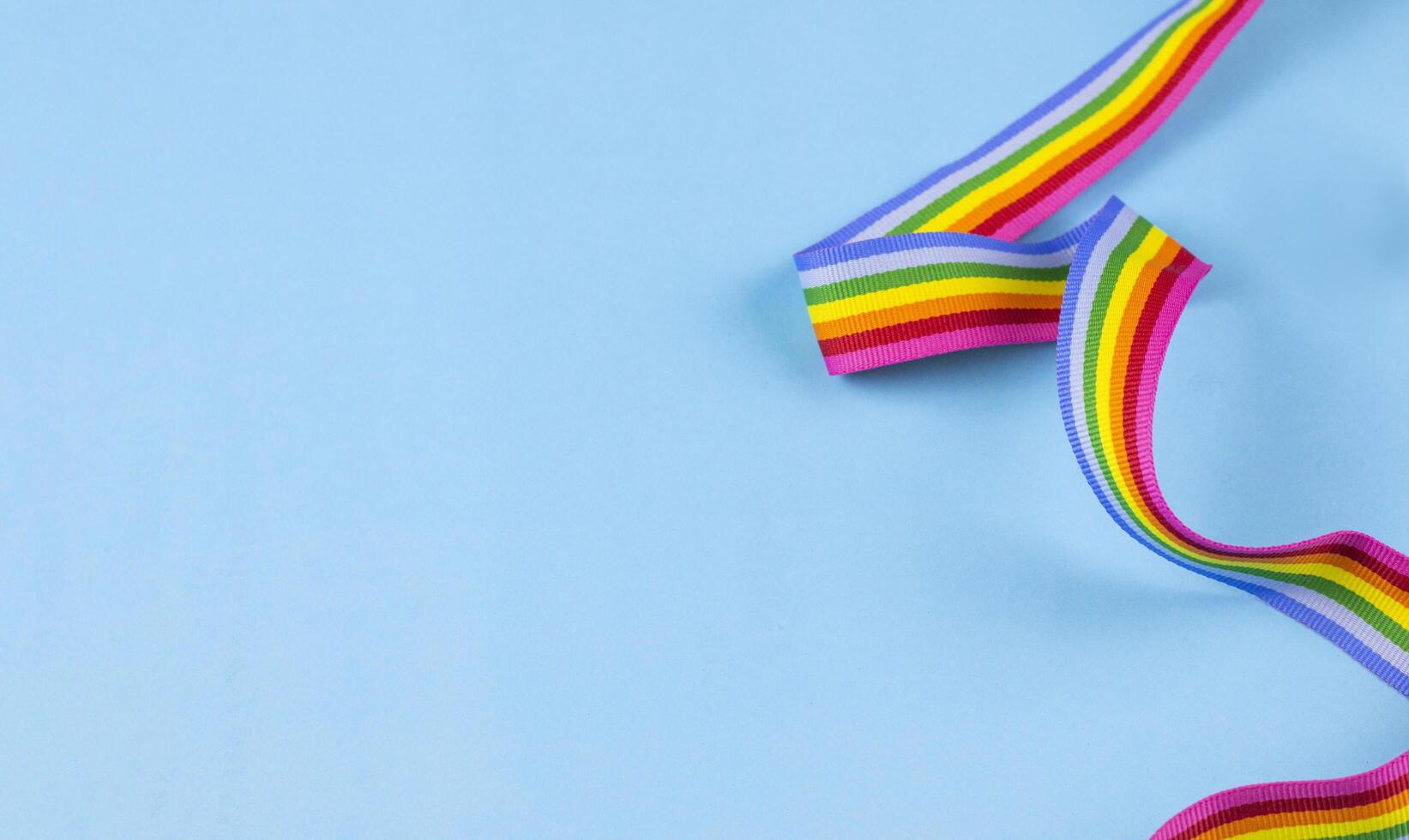 Colorful rainbow ribbon strip on blue pastel background. Concept of cheering LGBT communities all over the world photo