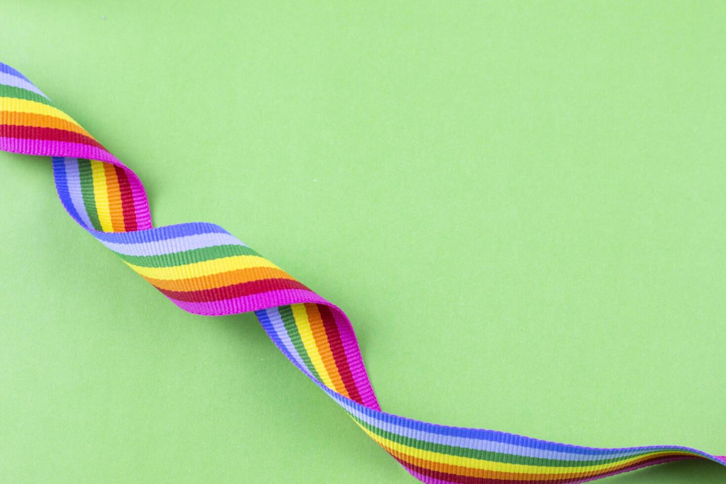 Colorful rainbow ribbon strip on green pastel background. Concept of cheering LGBT communities all over the world photo