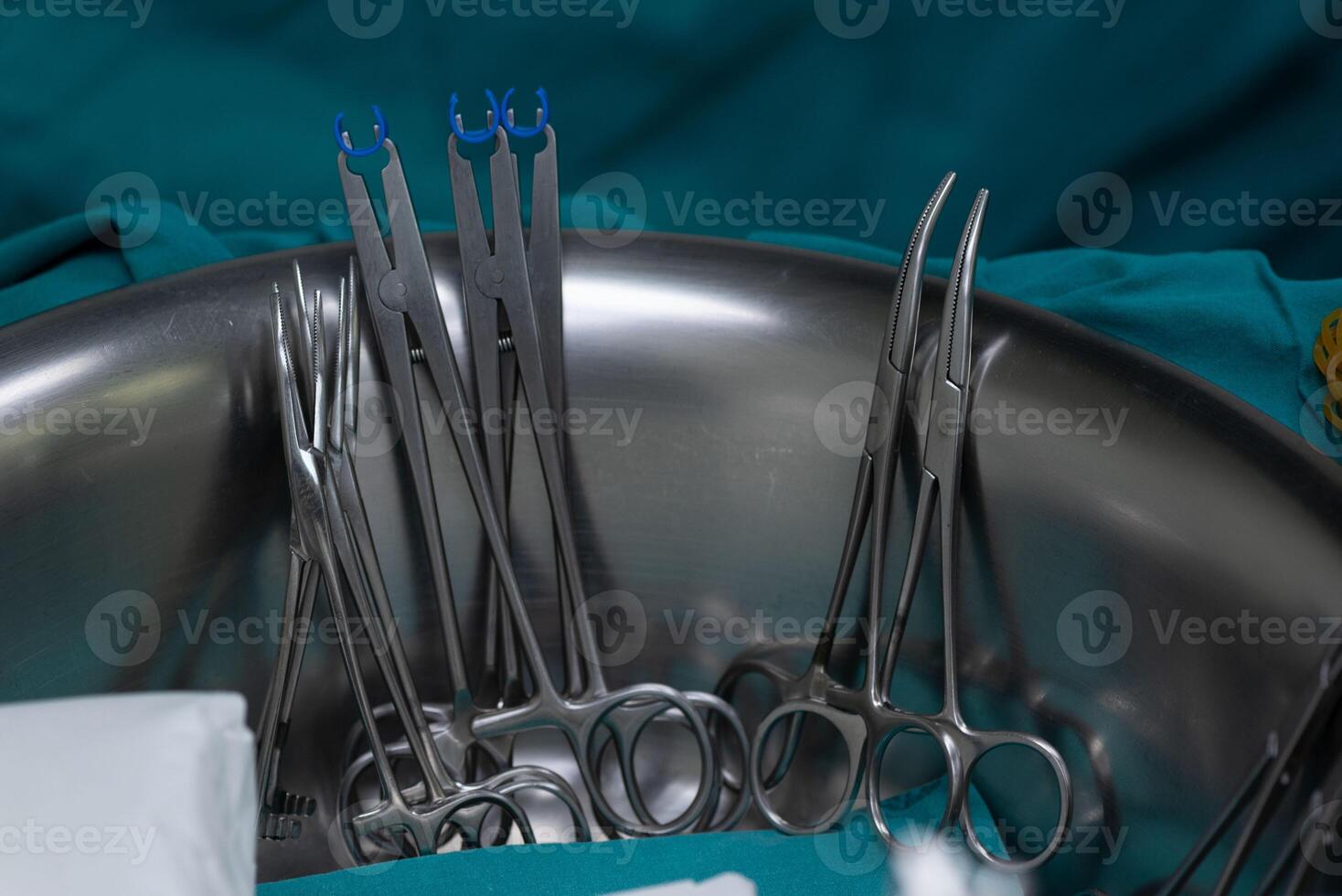Surgical clamps and forceps in stainless steel bowl on medical drape, prepared for medical procedure photo