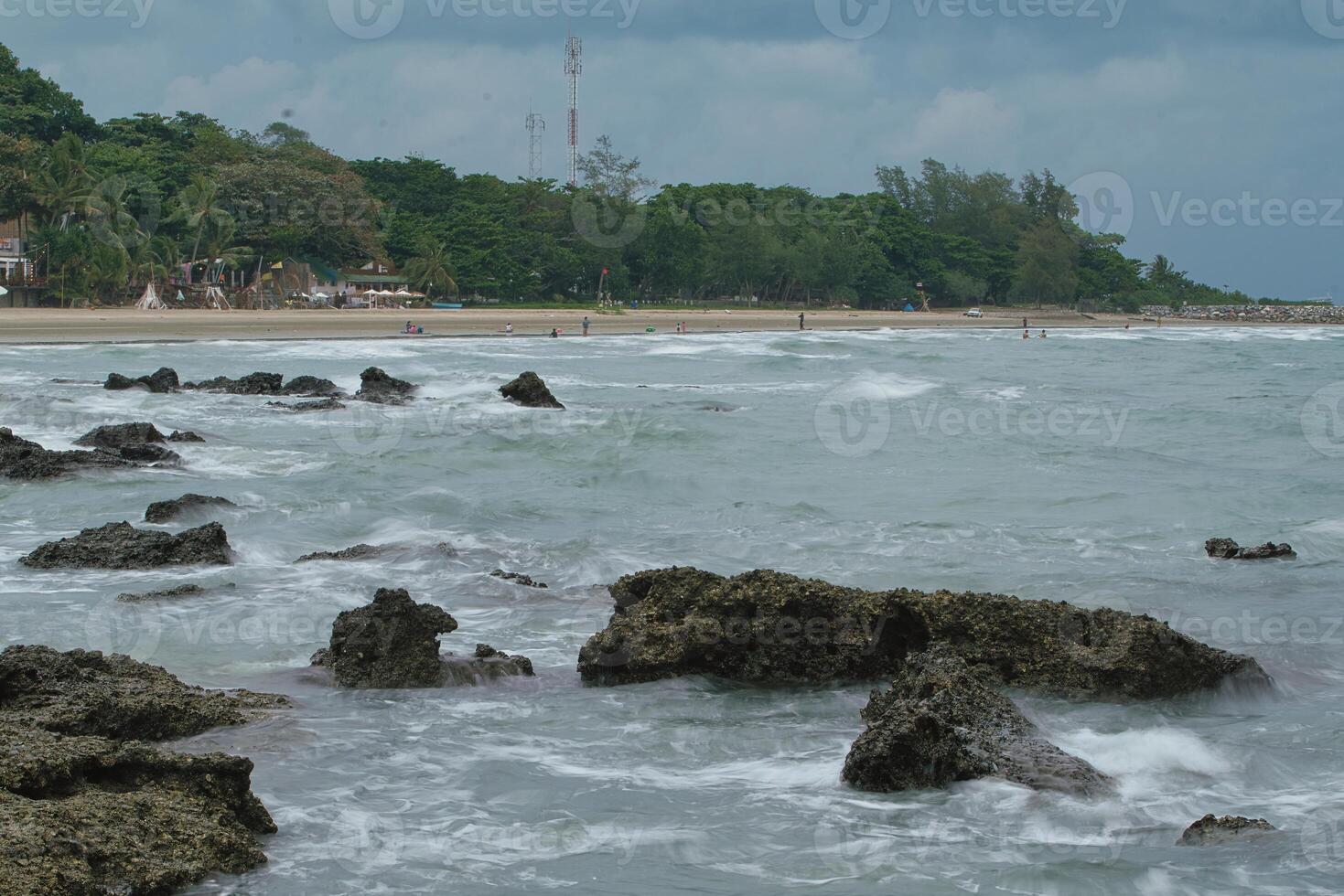 A beach with people playing in the water on a cloudy day photo
