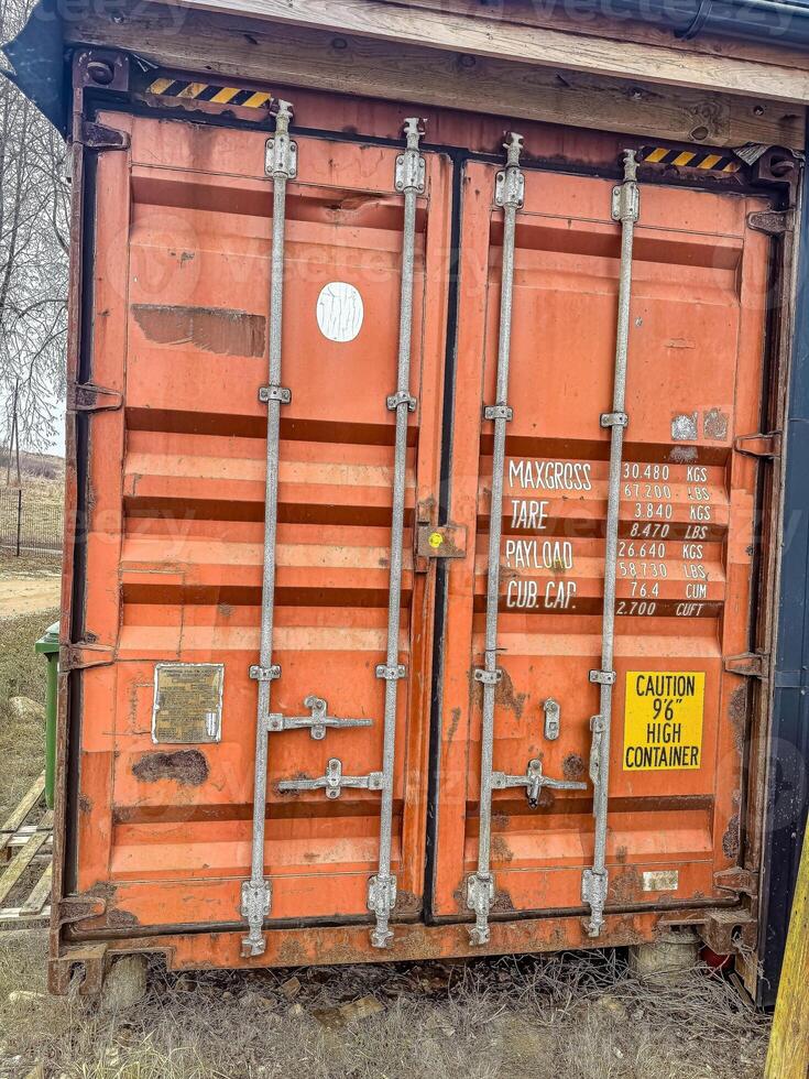 Orange shipping container with warning sign near rural area, showcasing cargo details and safety information on a clear day. High quality photo