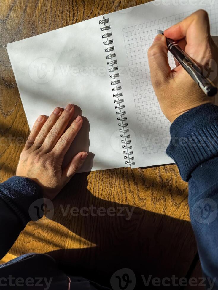 Close-up of hands writing IDEA in a notebook on a wooden desk in sunlight. High quality photo