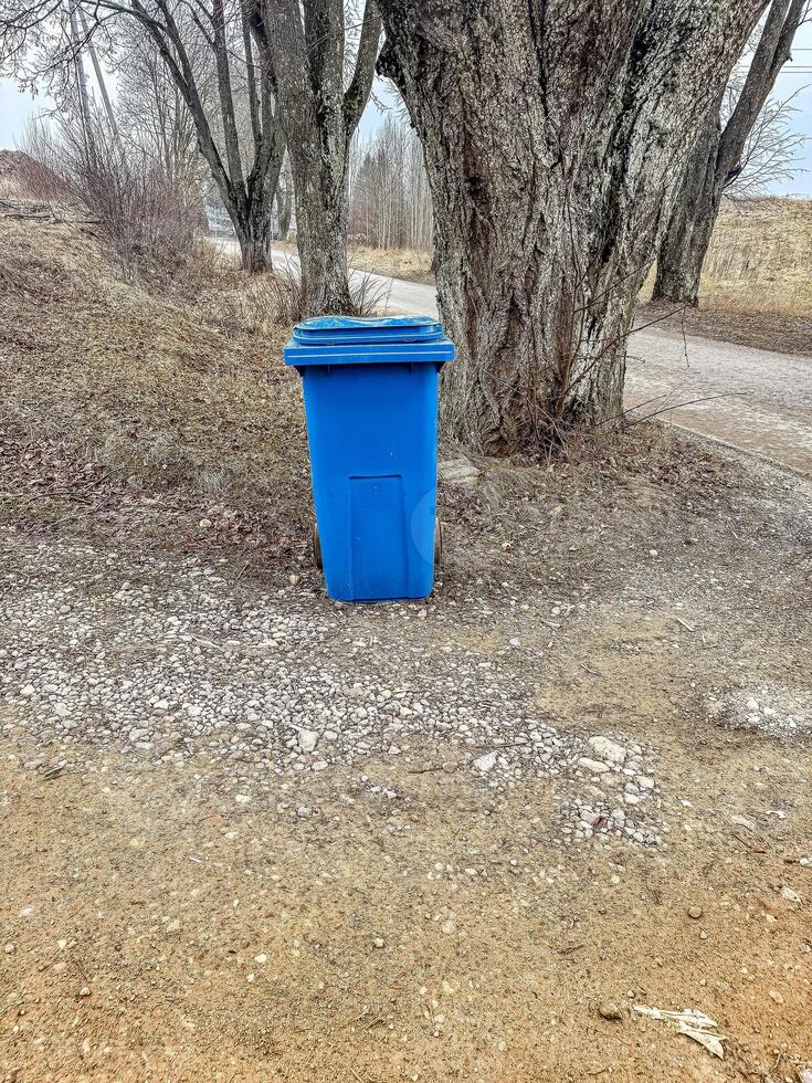 Blue Garbage Bin on Rural Gravel Path, Trees in Background, Outdoor Waste Management, Natural Setting. High quality photo