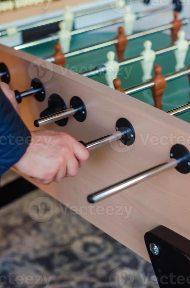 Close-up of a hand playing foosball, gripping the handle during a game match. High quality photo