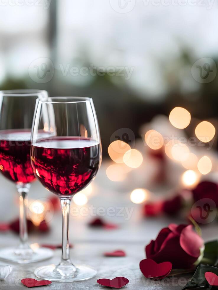 Two glasses of red wine with rose petals on the table photo